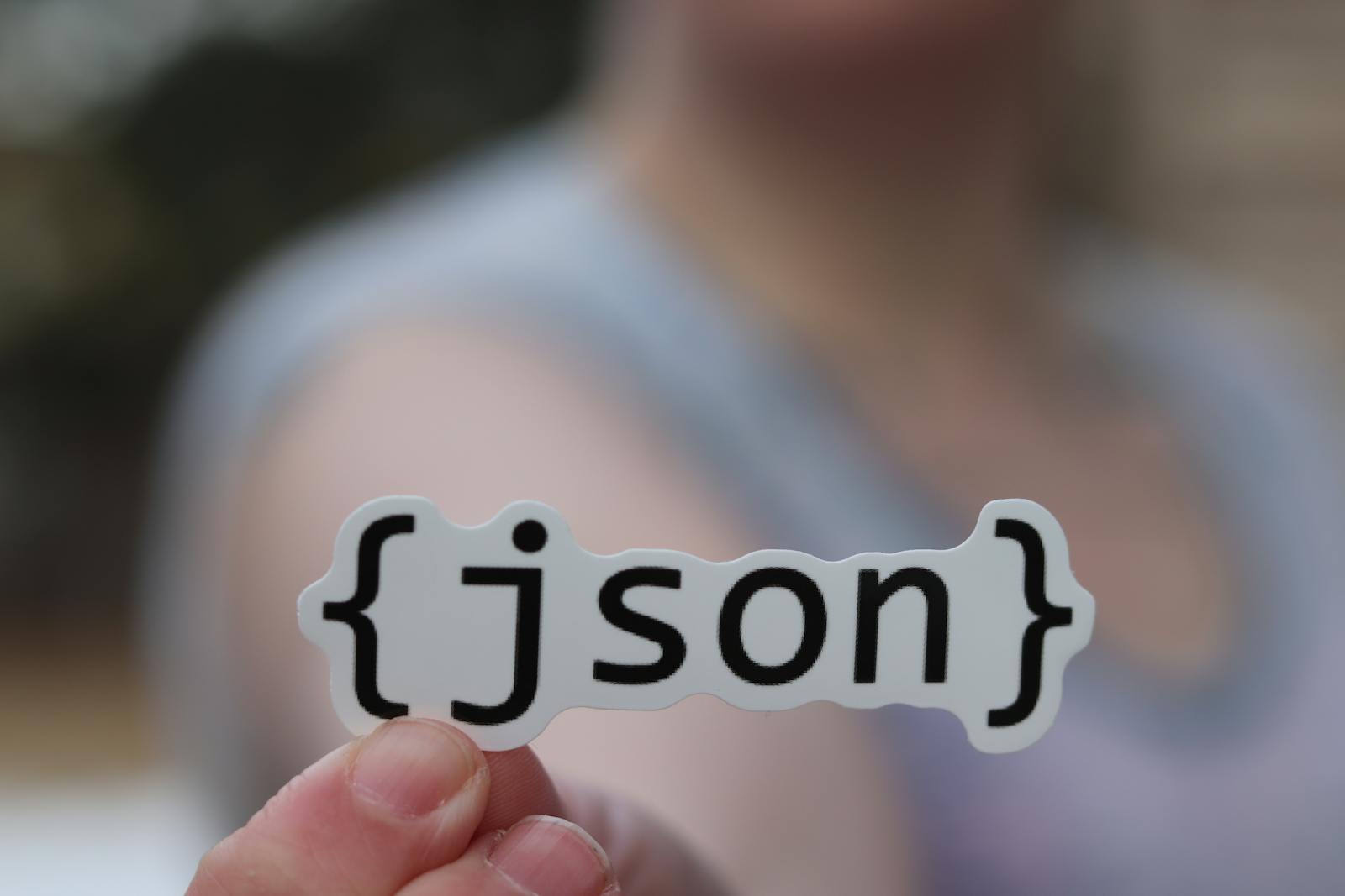 A hand holding a JSON text sticker, symbolic for software development.